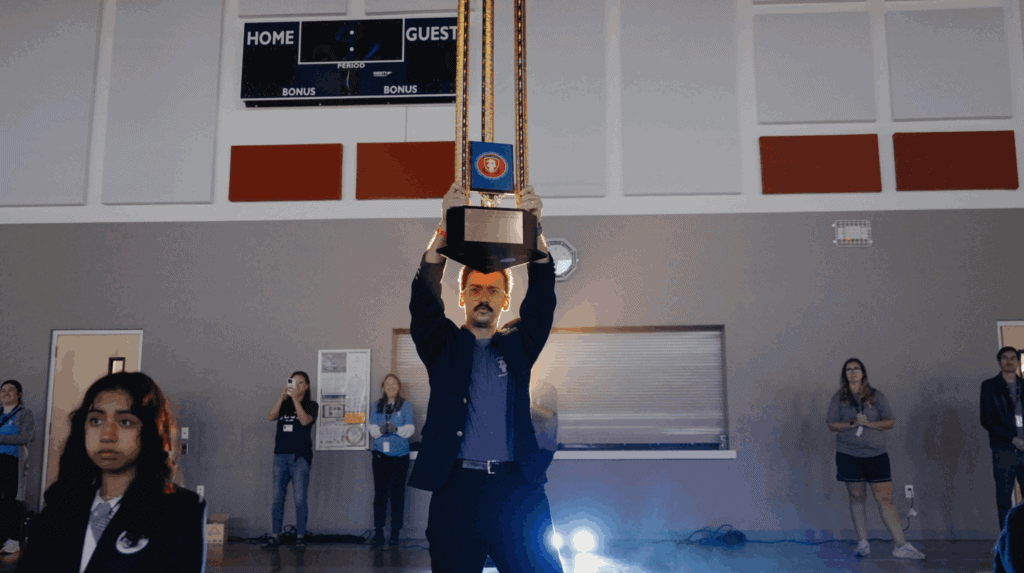 Man holding a trophy at an award ceremony in a gymnasium.